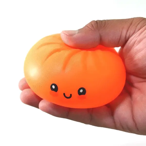 Mão apertando um squishy dumpling, mostrando a textura macia esticando e voltando à forma original